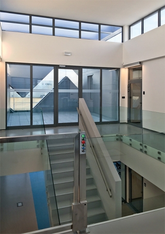 Pohled z interiéru nové centrály firmy Teco a.s. Za prosklenou stěnou je vidět logo firmy, které opticky prostupuje celou fasádou budovy.